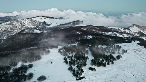 Snow-covered mountain landscape with misty forests and dramatic clouds