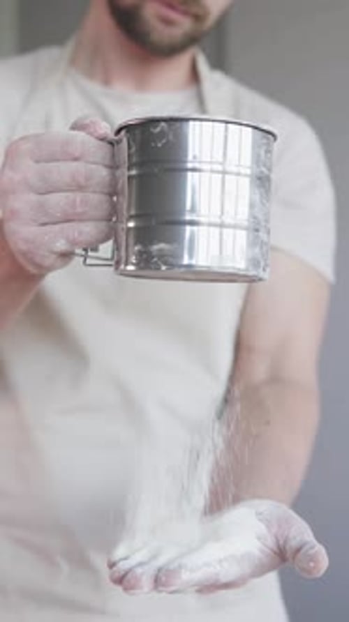 A cook in a bakery kitchen sifts flour through a sieve and begins to prepare bread. Vertical shot.