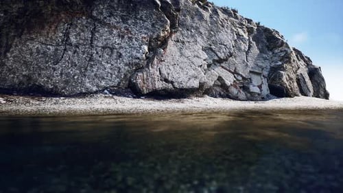 Rocky Shoreline with Clear Water and Blue Sky During Midday Sunlight