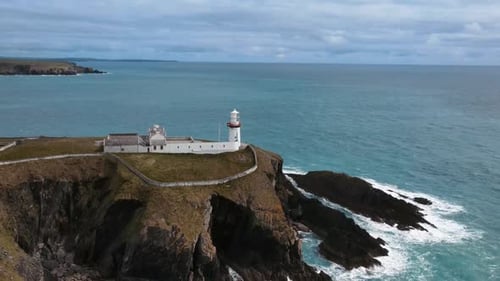 Drohne entfernt sich von einem weißen Leuchtturm über Felsen im Meer Irland