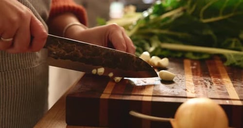 Adult Slicing Garlic Cloves on Cutting Board