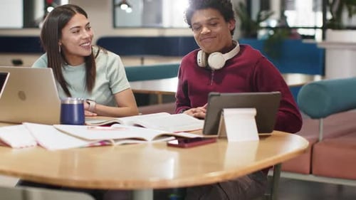 Étudiantes de sexe masculin étudiant à une table ronde pointant du doigt une tablette et retournant à un ordinateur portable