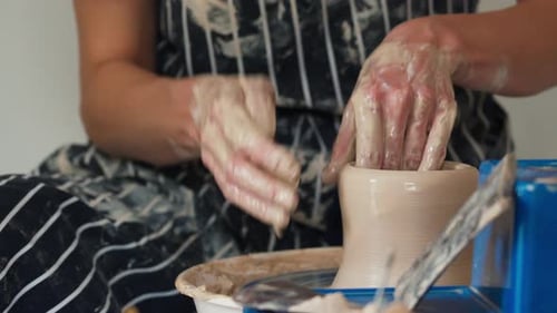 A female potter works on a potter's wheel, making a ceramic pot from clay in a pottery workshop.