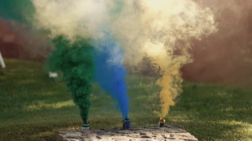 Colored smoke flares releasing green blue and yellow smoke outdoors
