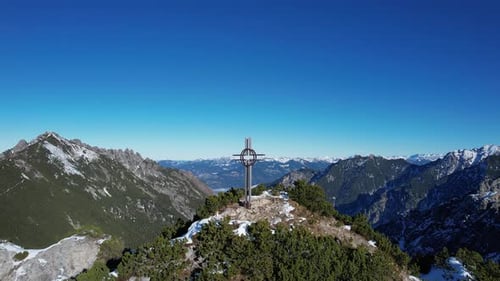 Aerial shot flying backwards with a stunning view on the summit cross on the mountain Alpspitz in Li