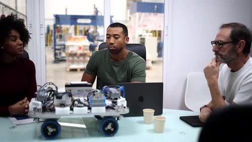 Multi generational and multiracial team of engineers developing a robotics project, using a laptop a