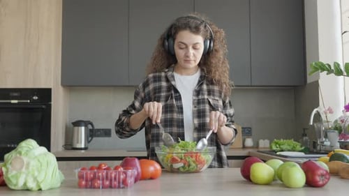 Woman with Headphones Prepares Salad in Kitchen