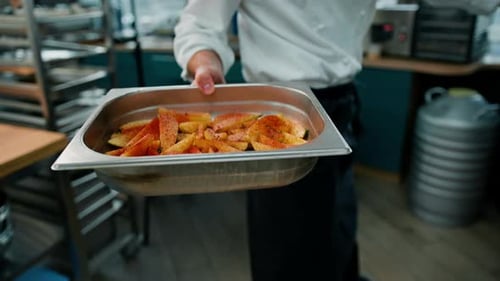 Professional kitchen chef who puts a baking sheet with pieces of raw potatoes with seasonings