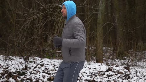 Young man jogging through a snowy winter forest in super slow motion