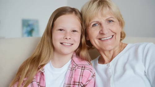 Happy Grandmother and Granddaughter Smiling Together on Couch