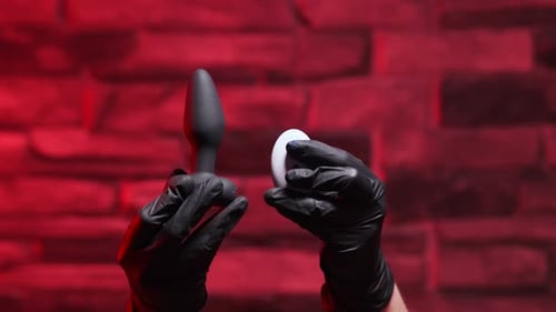 Analplug aus Silikon mit Fernbedienung dreht sich in einer weiblichen Hand in schwarzen Latexhandschuhen auf einem schwarzen B.