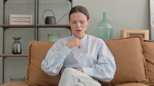 Young Adult Woman Coughing Indoors on Sofa