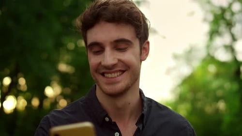 Portrait of Smiling Man Reading Message on Smartphone Outdoors. Closeup Cheerful Guy