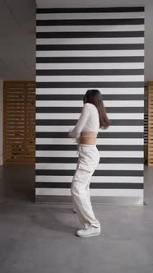 Stylish young woman performing an energetic street dance by a striped wall