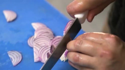Close-up of cutting onions with a kitchen knife on a blue cutting board.