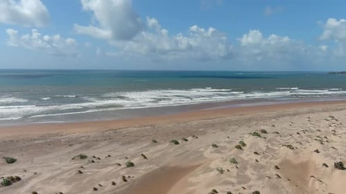 descending drone images to a beautiful large beach with light brown sand on a calm ocean