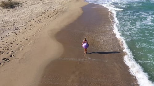 Blonde model woman walking on a beach aerial slow motion view. Sea waves washing sandy beach