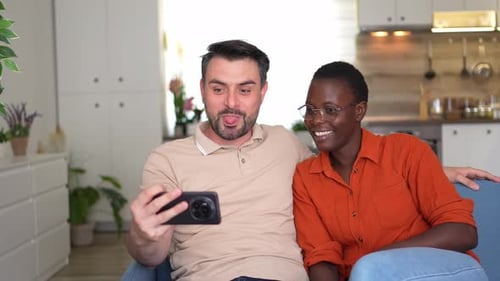 Smiling Couple Looks at Smartphone in Bright Home