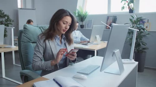 In Office Young Businesswoman Uses Phone Working on Laptop Computer On Background People Working
