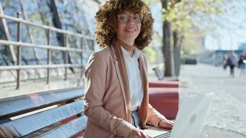 Woman Using Laptop on Bench in Sunny City Park