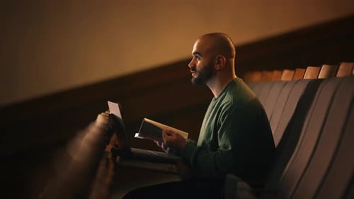 Student Flipping Through Notes and Typing on Laptop During University Lecture in Lecture Hall