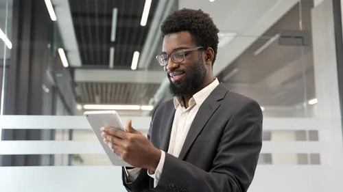 Smiling businessman holding digital tablet in modern business office. Confident black entrepreneur