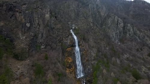 Aerial view of a majestic waterfall cascading down a steep, rocky cliff amidst a rugged mountain lan