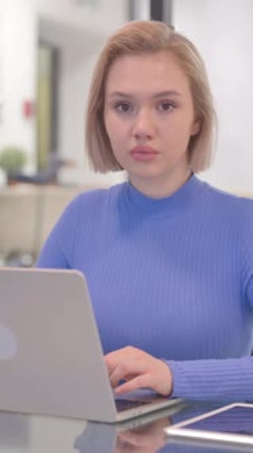 Young Woman Looking at Camera while Working on Laptop in Office, vertical video