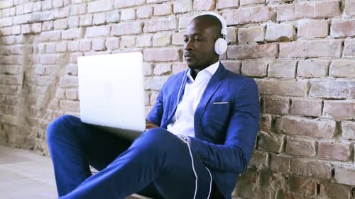 Man in Suit Using Laptop with Headphones