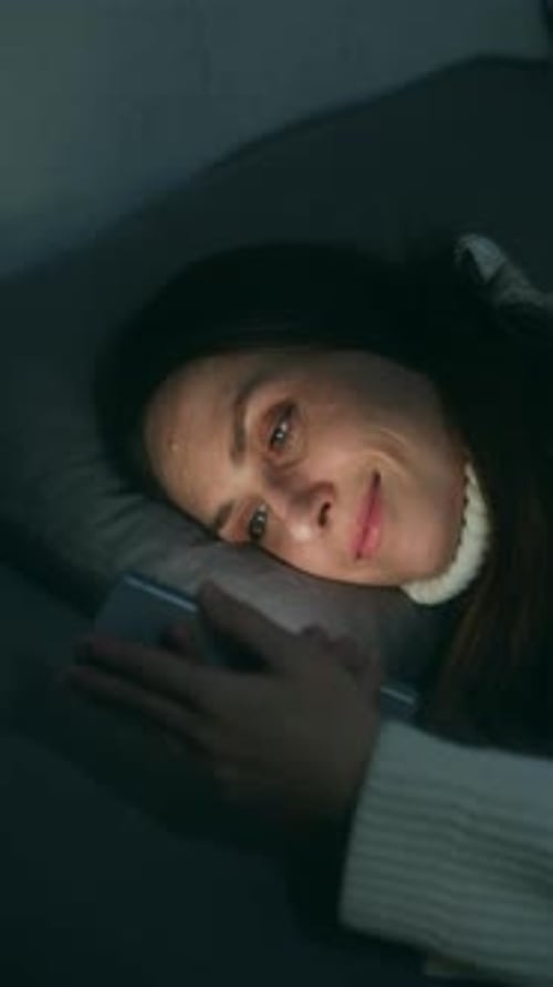 Woman Lies in Bed Looking at Smartphone