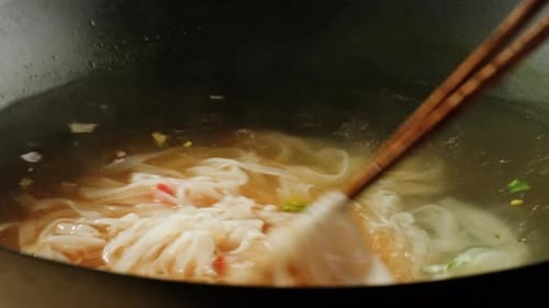 Noodles and Vegetables Stirred in Broth with Chopsticks