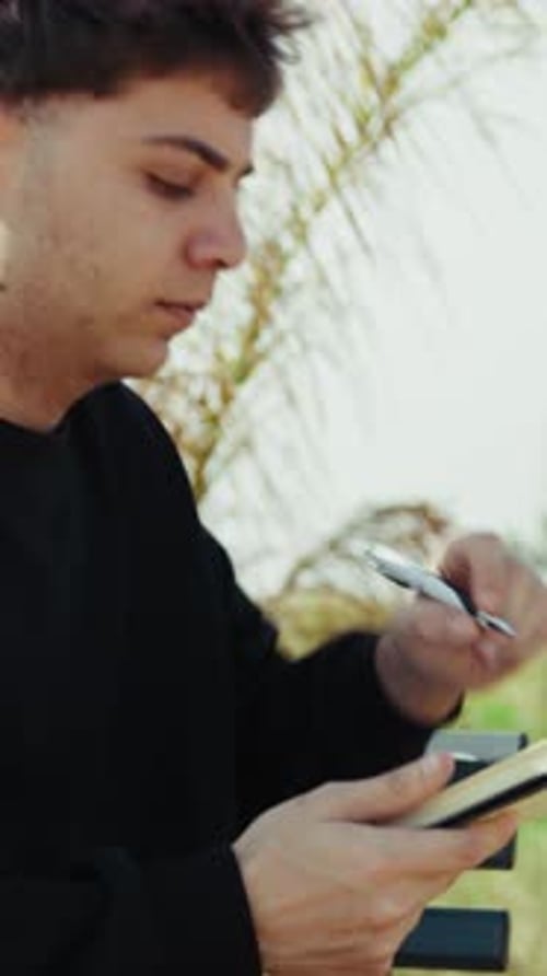 Young Student Writing Notes With A Pen While On The Park Bench