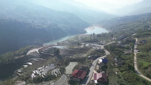 Aerial drone shot of villages amidst bright green rice terraces in the mountains of Sapa, Vietnam