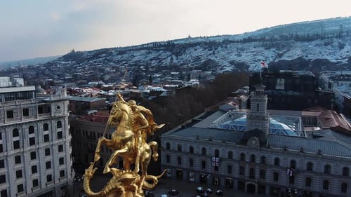 Aerial View of Golden Saint George Statue Overlooking SnowCapped Tbilisi Cityscape