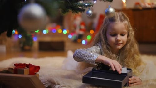 Little Girl Opening Gifts Under Christmas Tree