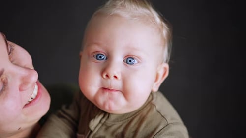 Sweet little Caucasian baby boy’s face with blue eyes. Woman is holding her beloved son. Close up.