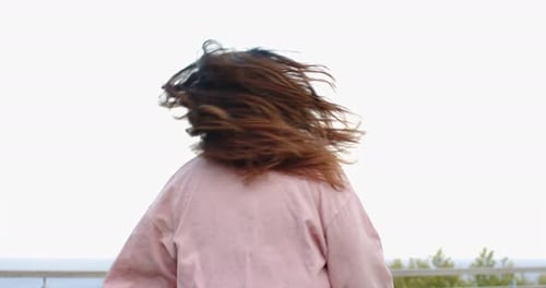 Hispanic woman catching breeze on balcony before spinning as pink overshirt billows and hair flips
