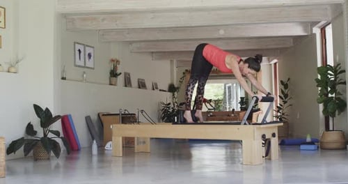 Fit senior caucasian woman stretching on reformer in pilates studio, unaltered, in slow motion