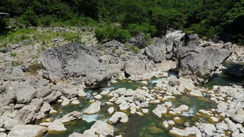 The drone steadily approaches a cluster of large river rocks, highlighting the rugged terrain and