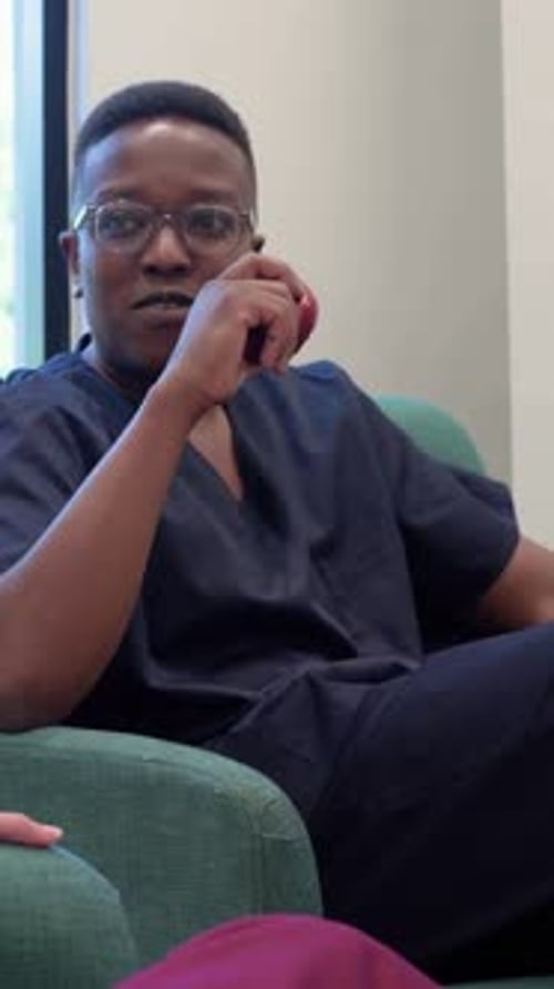 Vertical video: Picking red apple MD in navy scrubs biting accepting paper cup from peer in lounge