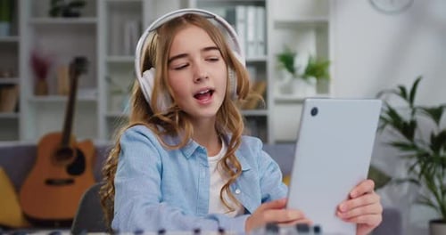 Retrato de una chica guapa de 10-11 años con el pelo largo y rizado en auriculares blancos escuchando música y cantando