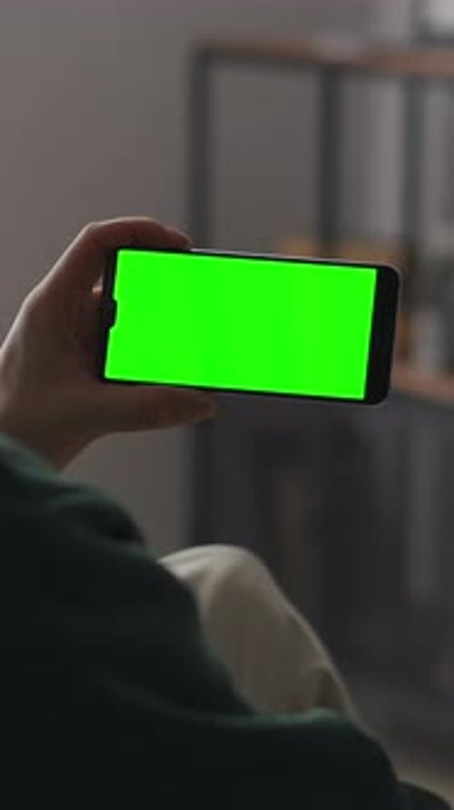 Person Holding Smartphone with Vivid Green Screen in Vertical and Horizontal Orientations Indoors