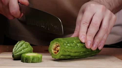 Couper une gourde amère sur un bureau en bois au couteau, gros plan d'un légume souvent utilisé comme ingrédient