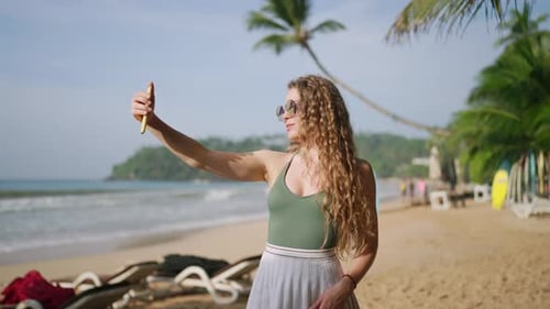 Attractive Woman Takes Selfies on Sandy Beach Waves in Background Sunglassclad Lady Snaps Photos