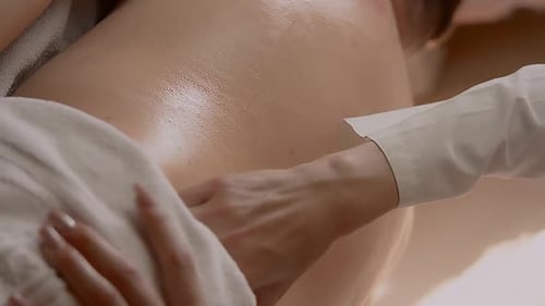 Young unrecognizable woman gets professional back massage in spa salon. Beautiful naked lady with pe