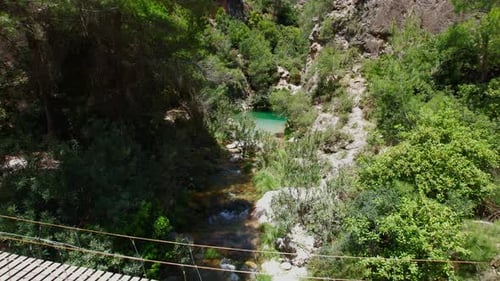 Hanging wooden walkway over a mountain stream with colorful turquoise waters. Aerial view at low alt