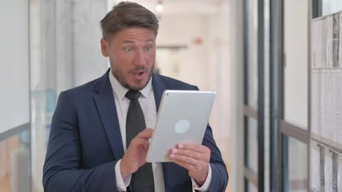 Excited Businessman Celebrating Success on Tablet in Office