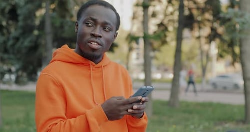 Man in Hoodie Uses Smartphone in City Park