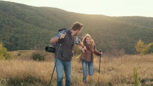 Smiling Couple Hiking Up Grassy Hillside Together
