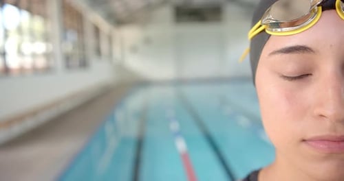Wearing swim cap and goggles, Female Swimmer standing by indoor pool, ready to swim, copy space